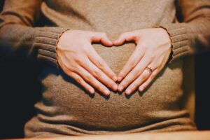 una dona incinta che mette le mani sulla pancia formando un cuore